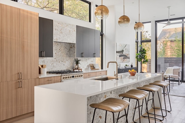 kitchen with an island with sink, hanging light fixtures, and stainless steel range oven