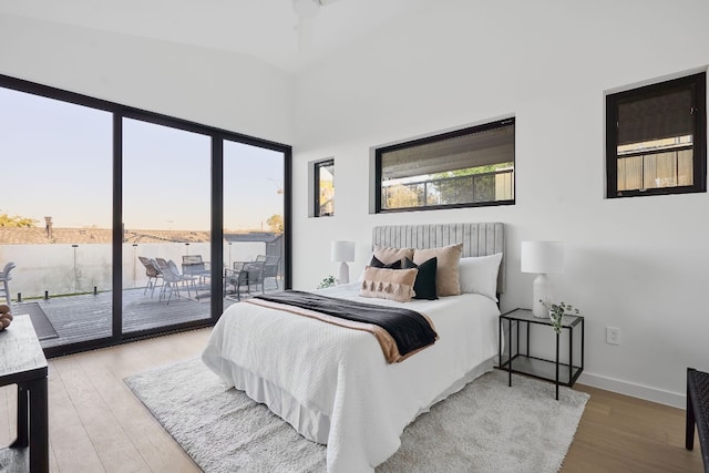 bedroom with light wood-type flooring, access to outside, vaulted ceiling, ceiling fan, and a water view