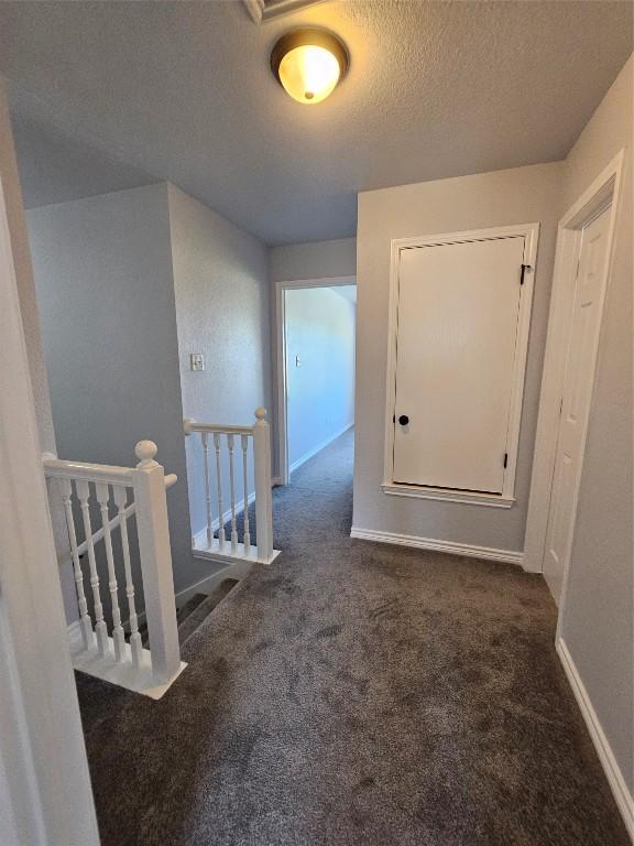 corridor featuring dark carpet and a textured ceiling