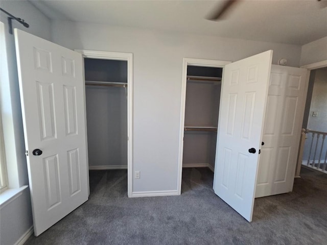 unfurnished bedroom featuring dark carpet, ceiling fan, and multiple closets