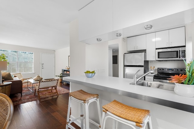 kitchen with a kitchen breakfast bar, dark hardwood / wood-style flooring, stainless steel appliances, sink, and white cabinetry