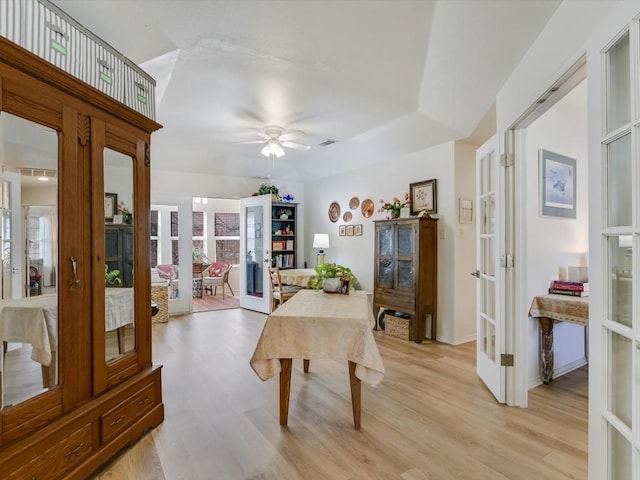 dining room with light wood-type flooring, a raised ceiling, ceiling fan, and french doors