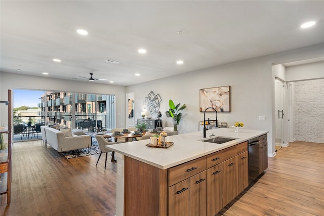 kitchen featuring light wood-type flooring, stainless steel dishwasher, ceiling fan, sink, and an island with sink