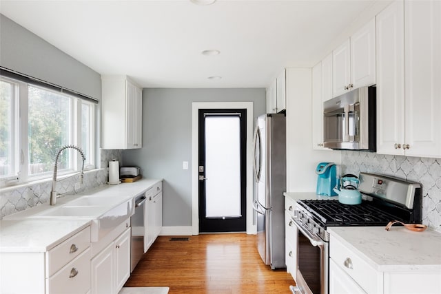 kitchen with white cabinets, sink, stainless steel appliances, and light hardwood / wood-style flooring