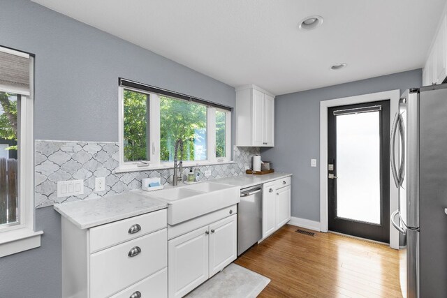 7611 Providence Ave Unit A, Austin, TX 78752 - kitchen featuring appliances with stainless steel finishes, light countertops, white cabinets, tasteful backsplash, and light wood-type flooring
