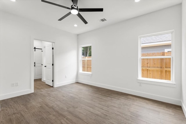 unfurnished bedroom with hardwood / wood-style flooring, ceiling fan, and a barn door