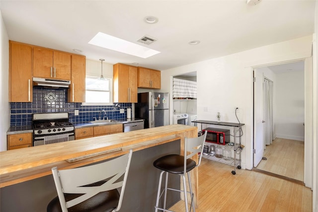 kitchen with light wood-type flooring, stainless steel appliances, independent washer and dryer, hanging light fixtures, and butcher block counters