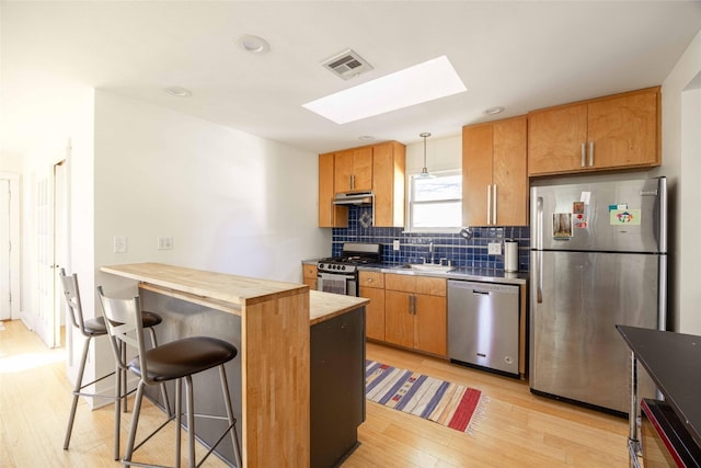 kitchen with a skylight, hanging light fixtures, wood counters, light hardwood / wood-style flooring, and appliances with stainless steel finishes