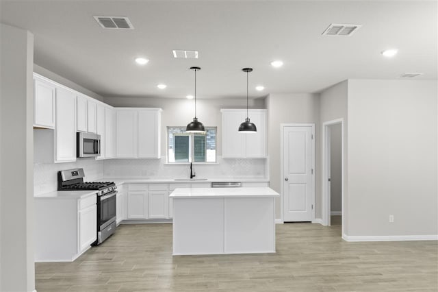 kitchen with pendant lighting, appliances with stainless steel finishes, a kitchen island, white cabinetry, and sink