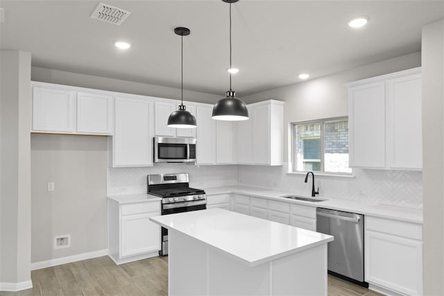 kitchen featuring white cabinetry, appliances with stainless steel finishes, hanging light fixtures, light hardwood / wood-style flooring, and a center island