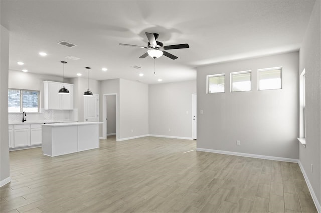 unfurnished living room featuring ceiling fan, light hardwood / wood-style floors, a wealth of natural light, and sink