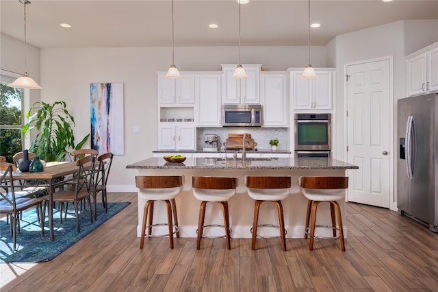 kitchen featuring appliances with stainless steel finishes, an island with sink, sink, dark stone countertops, and white cabinets