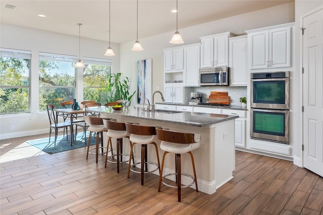 kitchen featuring appliances with stainless steel finishes, an island with sink, white cabinets, sink, and dark stone countertops