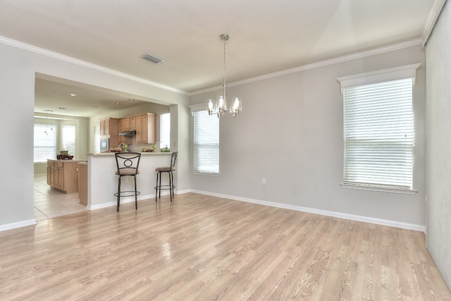 interior space with an inviting chandelier, a kitchen breakfast bar, kitchen peninsula, light wood-type flooring, and ornamental molding