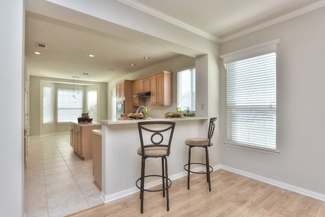 kitchen featuring stainless steel microwave, kitchen peninsula, light hardwood / wood-style floors, a kitchen bar, and ornamental molding