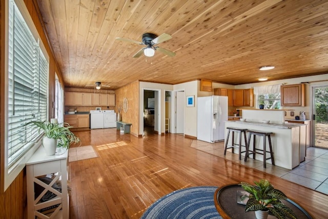 living room featuring ceiling fan, washing machine and clothes dryer, light wood-type flooring, and wooden ceiling