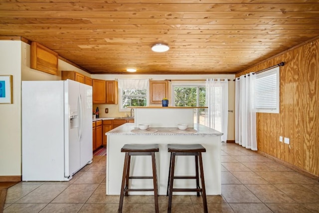 kitchen with wood ceiling, a center island, white fridge with ice dispenser, a kitchen bar, and wood walls