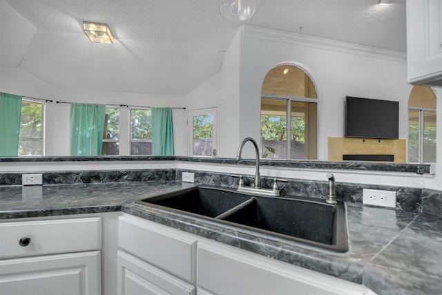 kitchen featuring lofted ceiling, white cabinets, sink, a fireplace, and a healthy amount of sunlight