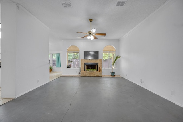 unfurnished living room featuring a textured ceiling, ceiling fan, crown molding, a tile fireplace, and concrete floors