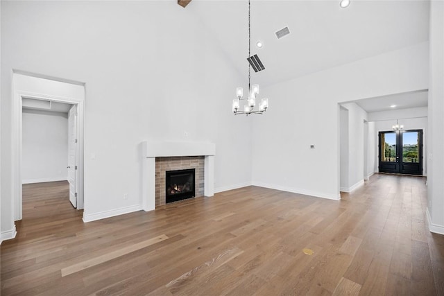 unfurnished living room with a fireplace, wood-type flooring, a chandelier, a high ceiling, and french doors