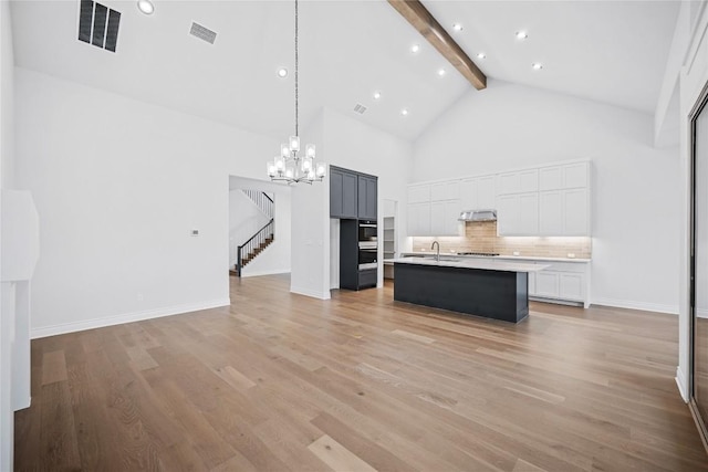 kitchen with high vaulted ceiling, an island with sink, sink, decorative backsplash, and beam ceiling