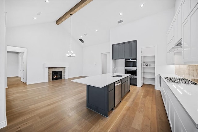 kitchen featuring tasteful backsplash, white cabinetry, sink, a kitchen island with sink, and beam ceiling