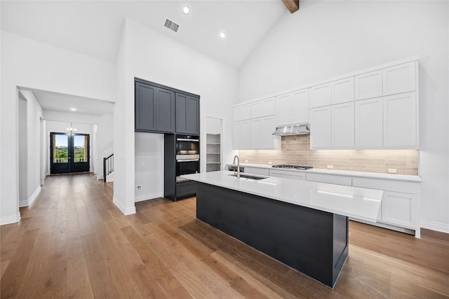 kitchen featuring sink, exhaust hood, beamed ceiling, a kitchen island with sink, and white cabinets