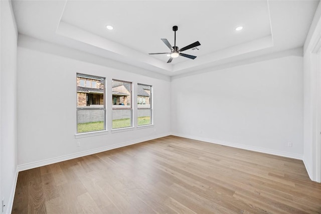 spare room with light hardwood / wood-style flooring, a raised ceiling, and ceiling fan