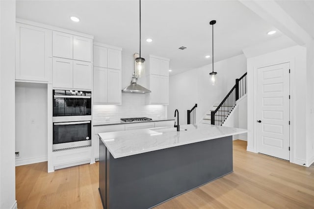 kitchen featuring white cabinets, stainless steel appliances, hanging light fixtures, and an island with sink