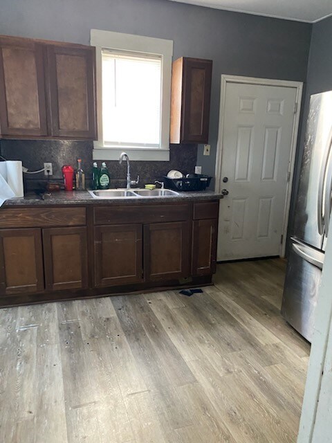 kitchen featuring light wood-type flooring, tasteful backsplash, dark brown cabinets, sink, and stainless steel refrigerator