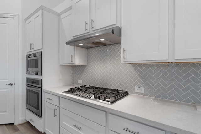 kitchen with decorative backsplash, white cabinets, light hardwood / wood-style floors, and appliances with stainless steel finishes