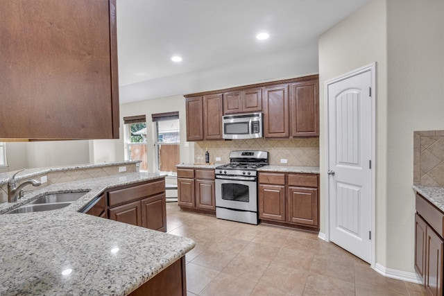 kitchen with sink, light stone countertops, light tile patterned floors, tasteful backsplash, and stainless steel appliances