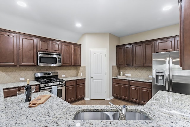 kitchen with decorative backsplash, stainless steel appliances, light stone counters, and sink