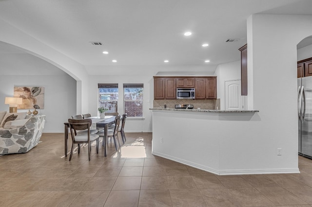 kitchen with light stone countertops, light tile patterned floors, tasteful backsplash, kitchen peninsula, and stainless steel appliances