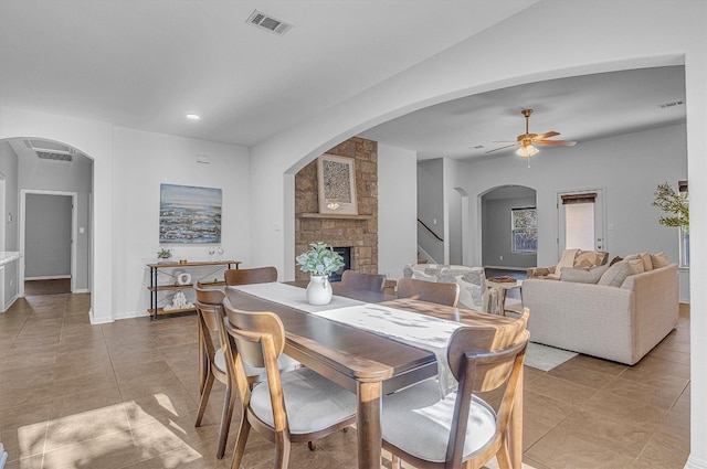 tiled dining space with a stone fireplace and ceiling fan