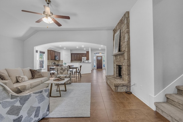 tiled living room with a stone fireplace, ceiling fan, and lofted ceiling