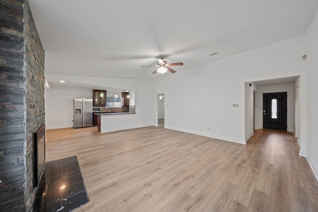 unfurnished living room with light hardwood / wood-style flooring, ceiling fan, and a stone fireplace