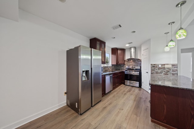 kitchen with kitchen peninsula, appliances with stainless steel finishes, wall chimney exhaust hood, sink, and light hardwood / wood-style floors