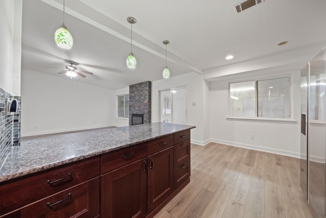 kitchen featuring pendant lighting, a stone fireplace, light wood-type flooring, and light stone counters