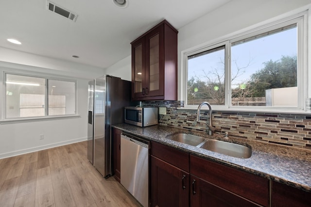 kitchen with appliances with stainless steel finishes, light wood-type flooring, backsplash, sink, and dark stone countertops