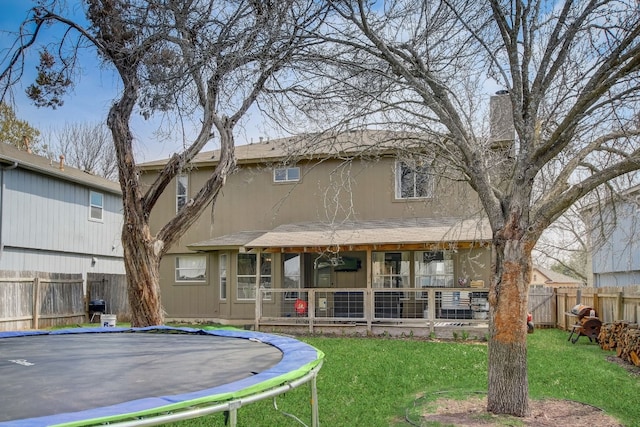 rear view of property with a trampoline and a lawn