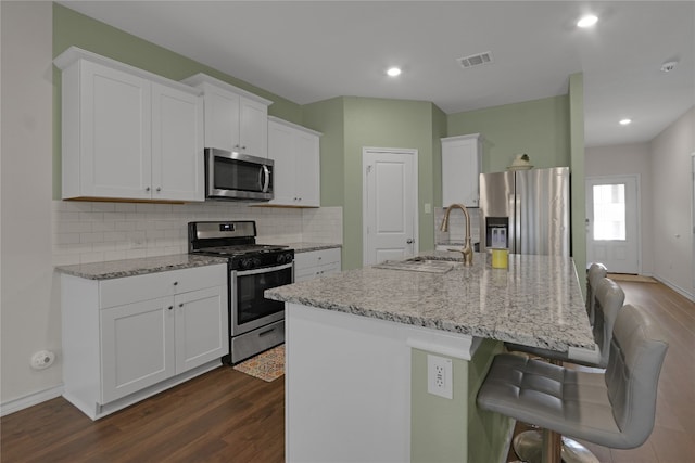 kitchen with dark wood-type flooring, stainless steel appliances, white cabinets, and a center island with sink