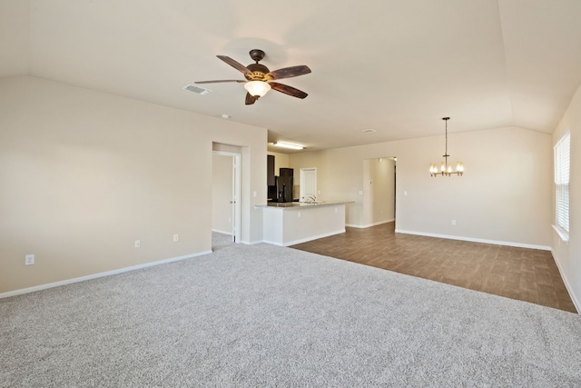 unfurnished living room featuring ceiling fan with notable chandelier, dark carpet, and lofted ceiling