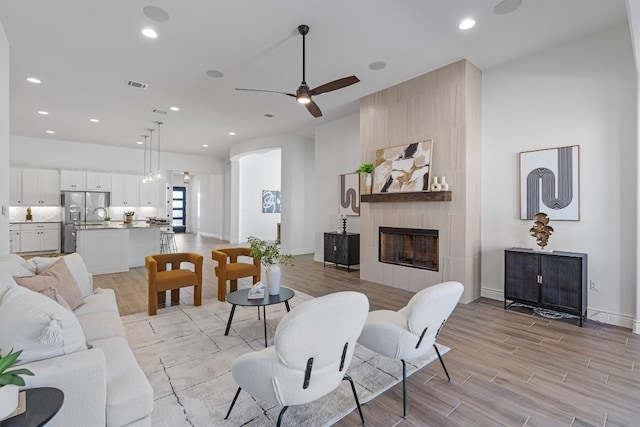 living room with a tile fireplace, light hardwood / wood-style floors, and ceiling fan