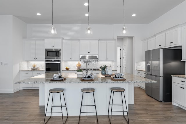 kitchen with appliances with stainless steel finishes, a center island with sink, white cabinetry, and hanging light fixtures