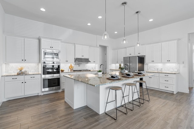 kitchen featuring stainless steel appliances, a kitchen island with sink, sink, light hardwood / wood-style flooring, and white cabinetry