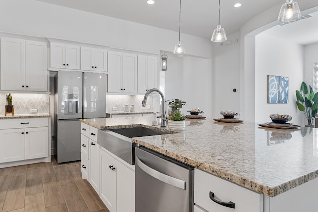 kitchen featuring decorative backsplash, appliances with stainless steel finishes, white cabinetry, and an island with sink