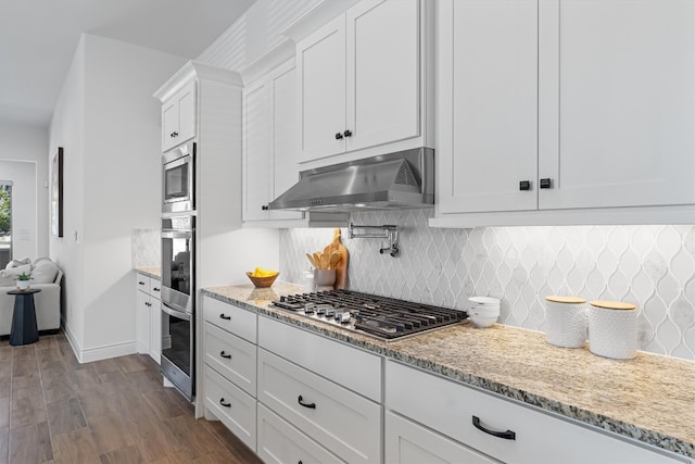 kitchen with tasteful backsplash, light stone counters, stainless steel appliances, white cabinets, and hardwood / wood-style floors