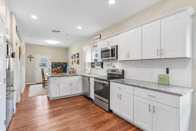 kitchen featuring hardwood / wood-style floors, sink, white cabinetry, kitchen peninsula, and stainless steel appliances