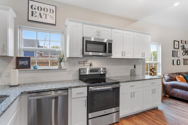 226 Spruce Ave, Luling, TX 78648 - kitchen with stainless steel appliances, white cabinetry, tasteful backsplash, light wood finished floors, and light stone counters